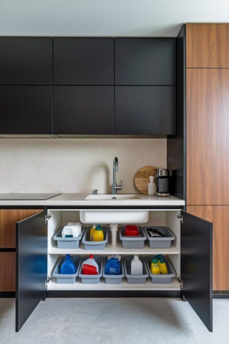 modern kitchen with black and wooden cabinets, and gray storage bins with cleaning supplies under the sink