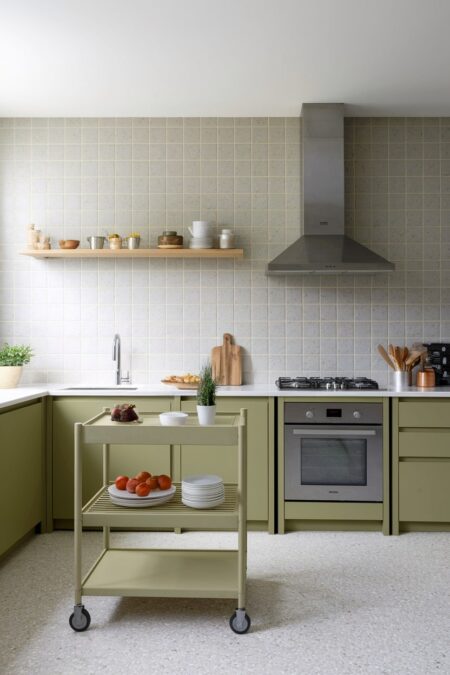 modern kitchen with green cabinets, light gray square tile backsplash, and a rolling kitchen cart with plates