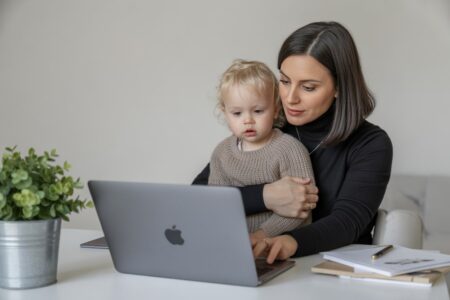 26 Side Hustles for Working Moms: Creative Ways to Secure Your Financial Future brunette mom working on a laptop while holding a child