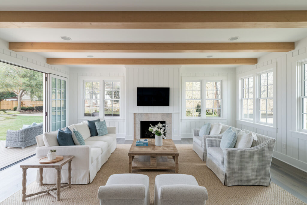 coastal style living room with lightwood ceiling beams, shiplap walls, and backyard doors