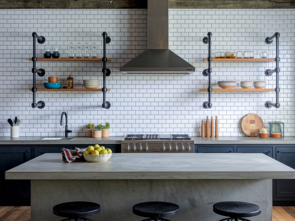 industrial style kitchen with open shelving of black iron pipes, white tile backsplash, and concrete island countertop