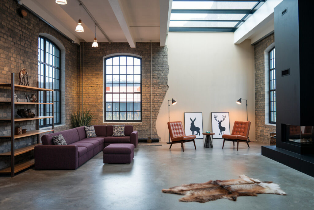industrial style living room with exposed brick walls, black fireplace, concrete flooring, and muted purple sectional sofa