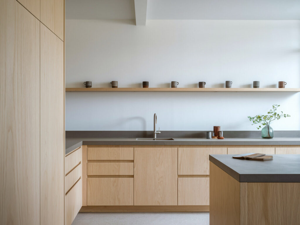 Japandi style kitchen with handle-less cabinetry in a light wood, open shelf with a collection of mismatched ceramic mugs