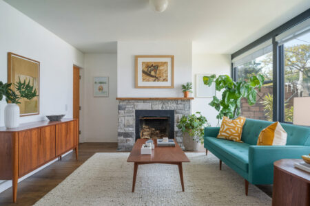 mid-century modern living room with white walls, stone fireplace, wooden console and coffee table