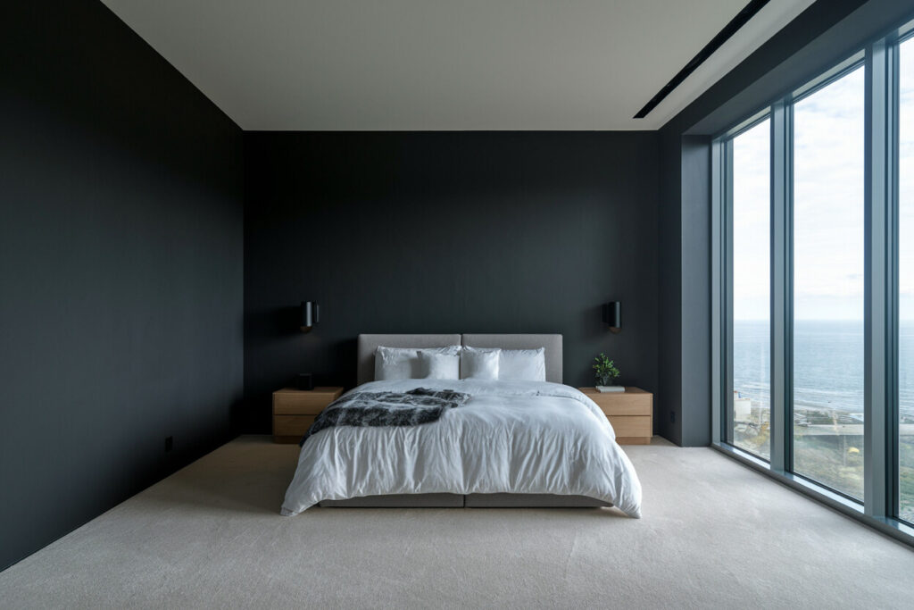 minimalist bedroom with dark gray walls, light wood nightstands, floor-to-ceiling windows