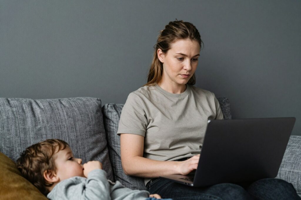 mom works on laptop while sitting on a gray sofa at home