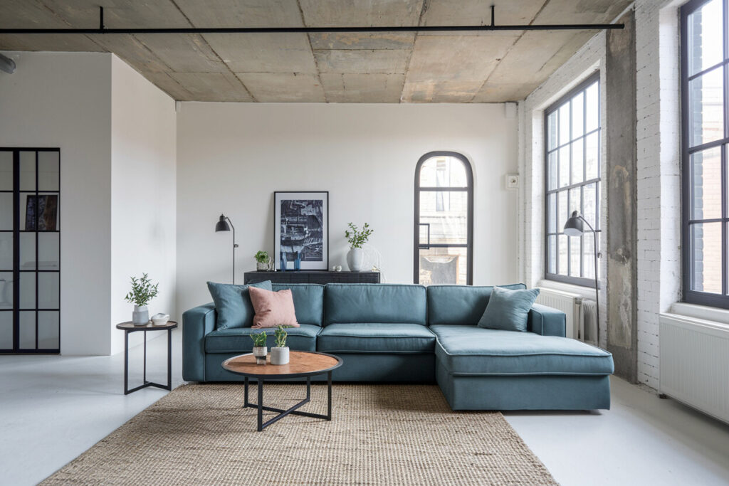 open plan industrial style living room with white walls, concrete ceiling, muted blue sectional sofa, and black accents