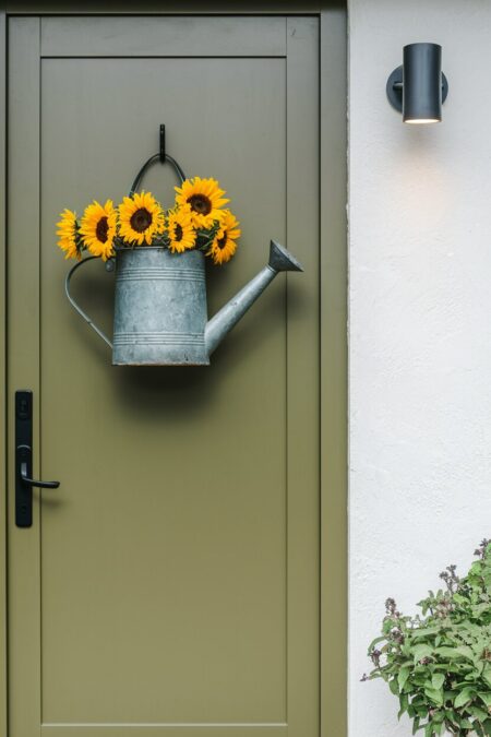vintage watering can with sunflowers on the olive green front door as summer decor