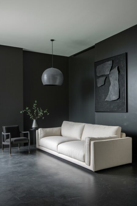 contemporary dark living room with charcoal concrete flooring, a low-profile oatmeal sofa, oversized pendant light, and an abstract wall art