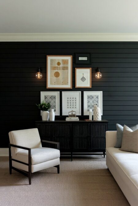 dark living room with a black accent wall featuring a gallery of framed artwork and light seating