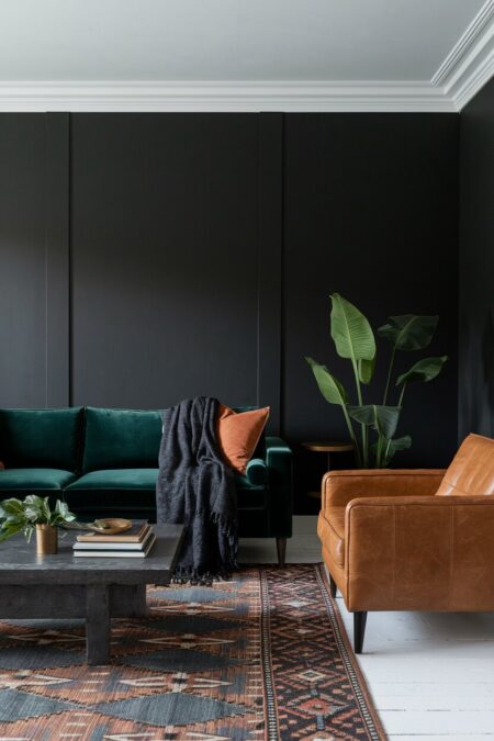 dark living room with a forest green velvet sofa and cognac leather armchair, patterned kilim rug