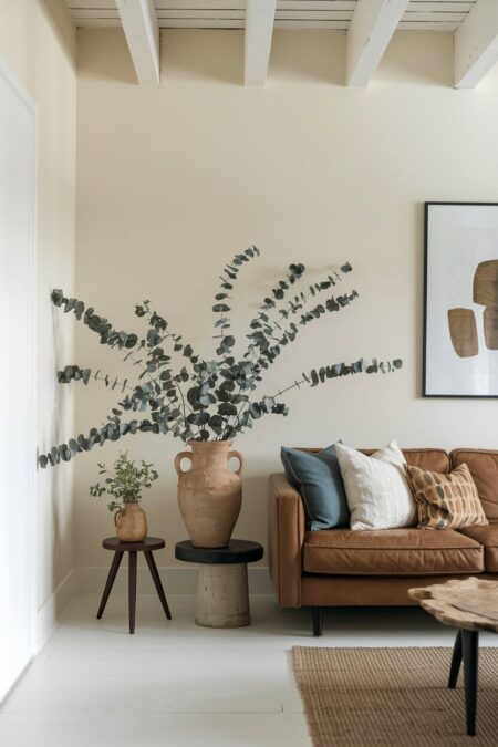 earthy living room with branches of eucalyptus in a earthenware vase on the side table and a leather couch