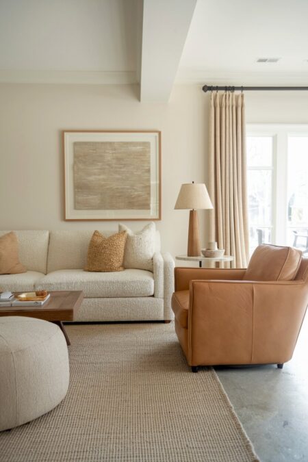 earthy living room with warm white walls, a cream boucle sofa, and a camel leather armchair