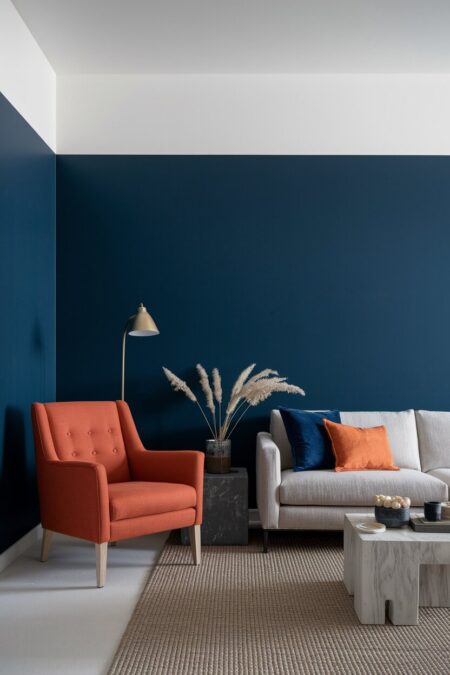 modern living room with navy blue walls, a burnt orange armchair, and a light neutral sofa