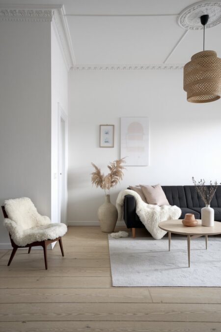 Scandinavian neutral living room with white walls, blonde wood floors, a charcoal sofa, and sheepskin throws