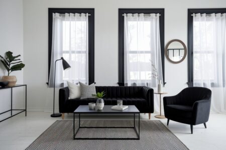 black and white living room with a velvet sofa and armchair, black window trim, white walls and flooring