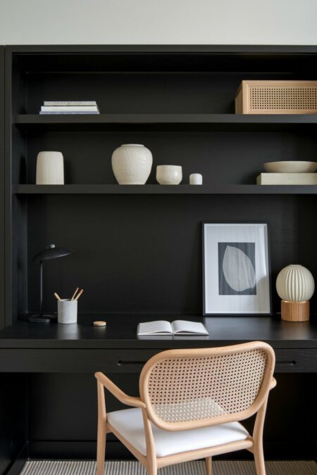Japandi black home office with rattan accents, a ceramic pen cup, a small sculptural lamp, a framed print