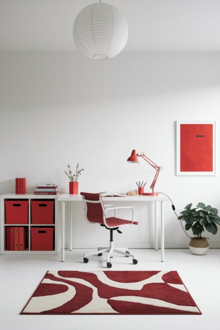 minimalist home office with white walls, a red desk lamp, storage boxes, office chair, and a printed rug