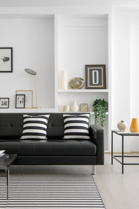 modern living room with white walls, a black leather sofa, black and white stripes on the throw pillows and rug