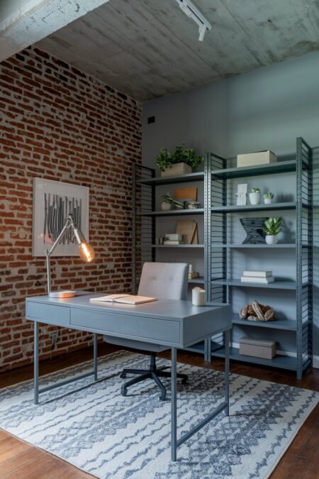 industrial gray home office with an exposed brick wall, a gray metal desk, and industrial shelving units