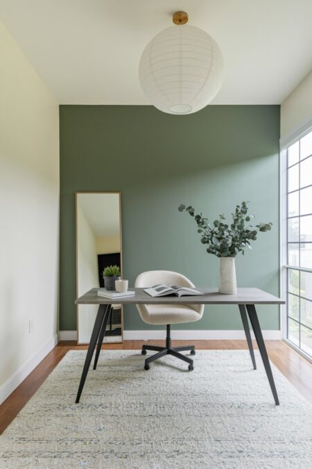 minimalist home office with a sage green accent wall behind the desk and a mirror on the floor