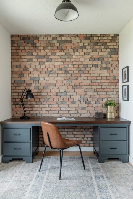 small industrial home office with an exposed brick accent wall, leather chair, and a wooden desk with gray drawers