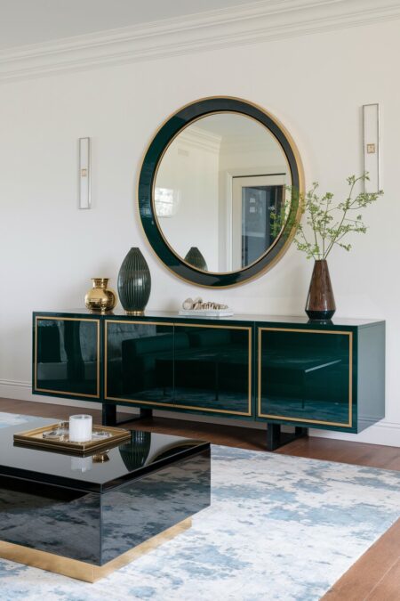 Art Deco living room with white walls, a glossy black coffee table, and a deep emerald sideboard