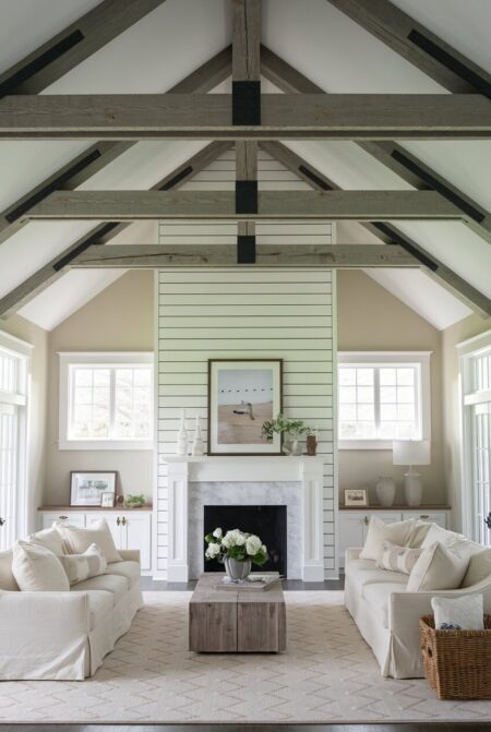farmhouse living room has vaulted ceiling with wood beams, beige walls, and shiplap behind the fireplace
