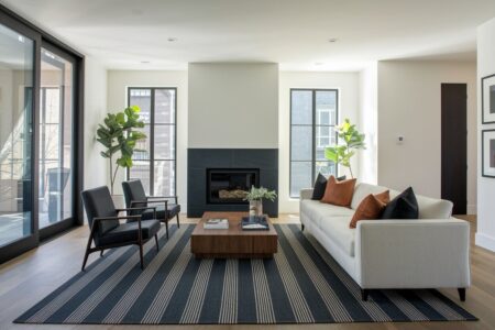 11 Masculine Living Room Ideas Rooted in Clean Lines masculine living room with white walls, a fireplace, a cream sofa, two black accent chairs, and a dark striped rug