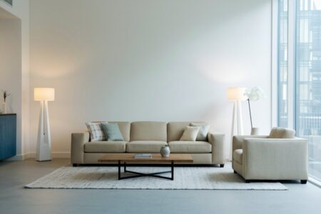 minimalist living room with white walls, a couch, upholstered armchair, and two floor lamps