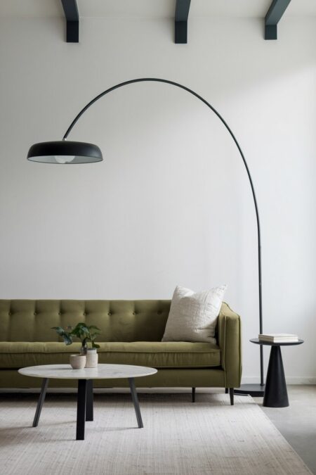 minimalist living room with white walls, a green sofa, and a black arc floor lamp