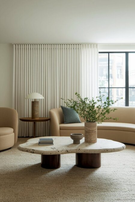 modern living room with a beige sofa, floor-to-ceiling curtains, and a sculptural stone coffee table