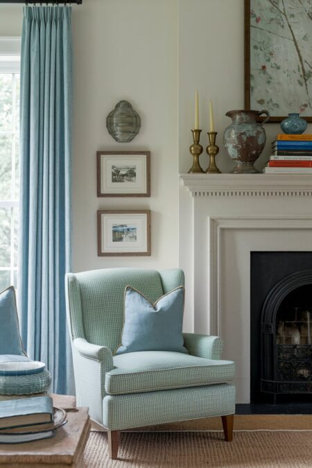 vintage living room with a light green armchair, light blue curtains, an old pitcher and brass candlesticks on the mantel