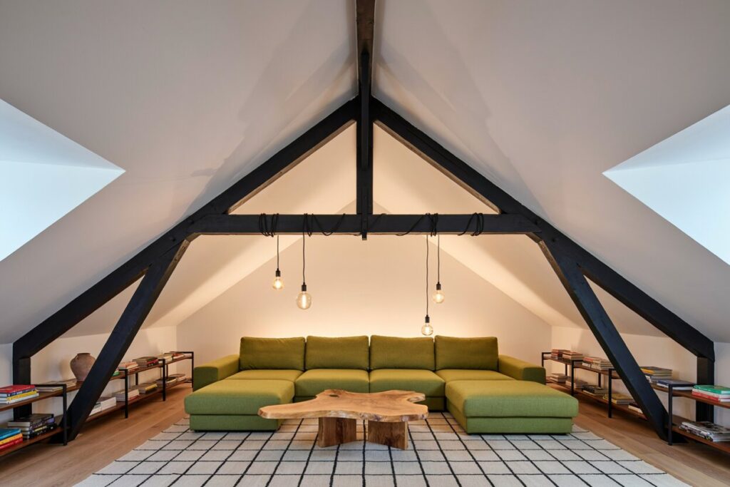 attic living room with black ceiling beams, a green sectional sofa, a wooden coffee table, and open shelving with black metal frame