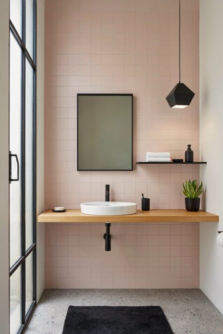 bathroom with pale pink square wall tiles, black fixtures, black decor, and a floating wood vanity shelf