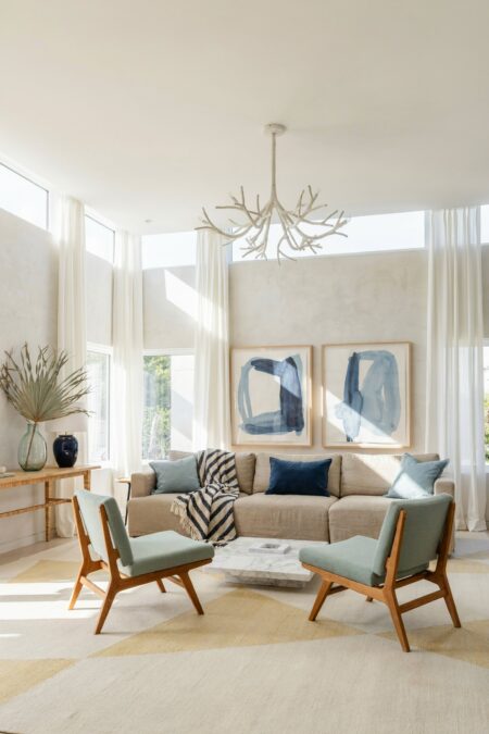 modern beach house living room with light seafoam accent chairs, an oatmeal sofa, a navy velvet cushion, two abstract paintings in deep navy and light aqua blue, and a sculptural branch-like chandelier