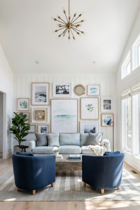 beach house living room with a seaside gallery wall, navy blue barrel chairs, a brass sputnik chandelier, and a light blue sofa