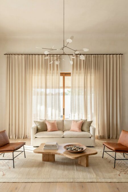 beach house living room with soft oatmeal sheer linen curtains, a cream sofa, leather chairs, and a bowl with sea stones on the coffee table