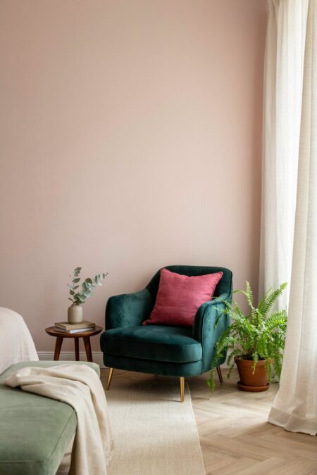 bedroom with blush walls, an emerald green velvet chair with a pink throw pillow and a leafy fern next to it; a sage green bedroom bench