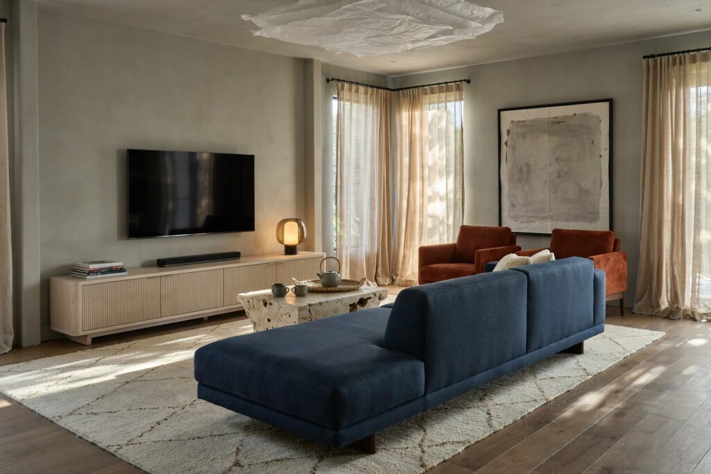 contemporary Japandi living room with greige walls, a slate blue sofa, and rust armchairs in corduroy fabric