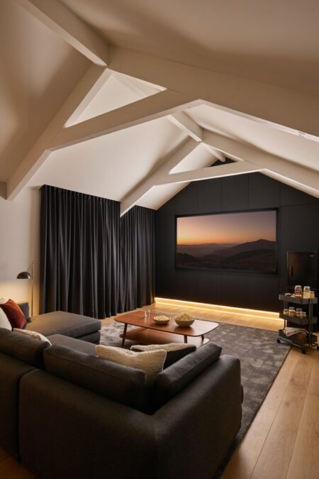 cozy attic media lounge and home theater with a gray sofa, mini fridge, and a snack cart