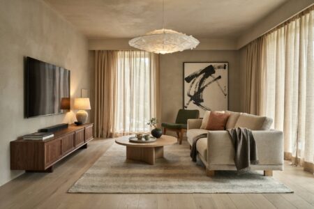 Japandi living room with limestone plaster on walls, a moss green accent chair, a linen sofa, a walnut media console, and a small bonsai on the coffee table