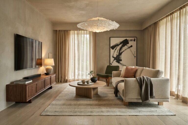 Japandi living room with limestone plaster on walls, a moss green accent chair, a linen sofa, a walnut media console, and a small bonsai on the coffee table