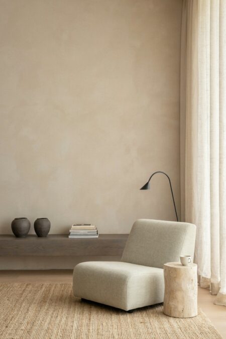 Japandi living room has a low gray open shelf with dark gray stoneware vases and a stack of books, a low lounge chair, and a minimalist black floor lamp