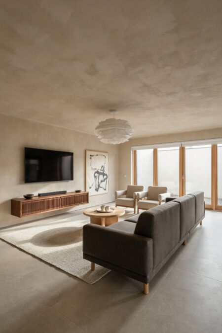Japandi living room with soft-beige clay plaster walls, a gray low-profile sofa, a floating media console, and compact oatmeal armchairs