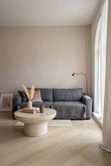 living room with a pale blush wall with beige undertone, a gray sofa, light wood flooring, and a travertine coffee table