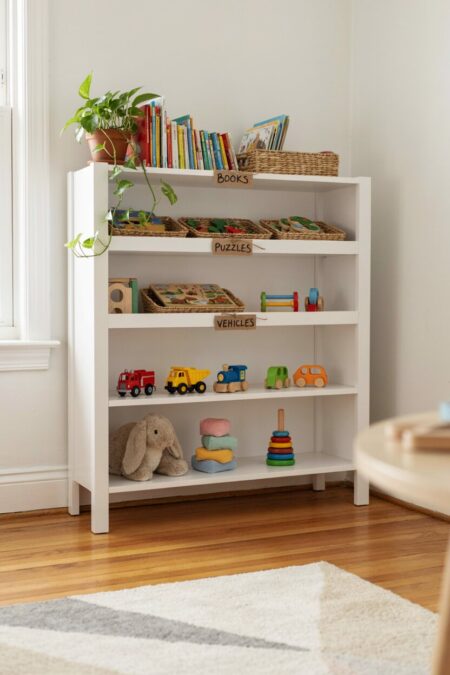 low, plain white bookcase with grouped toys by categories like puzzles and vehicles