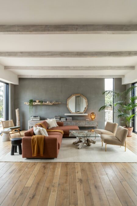 modern beach house living room with driftwood accents, a terracotta sectional sofa, two lounge chairs, and gray limewash walls