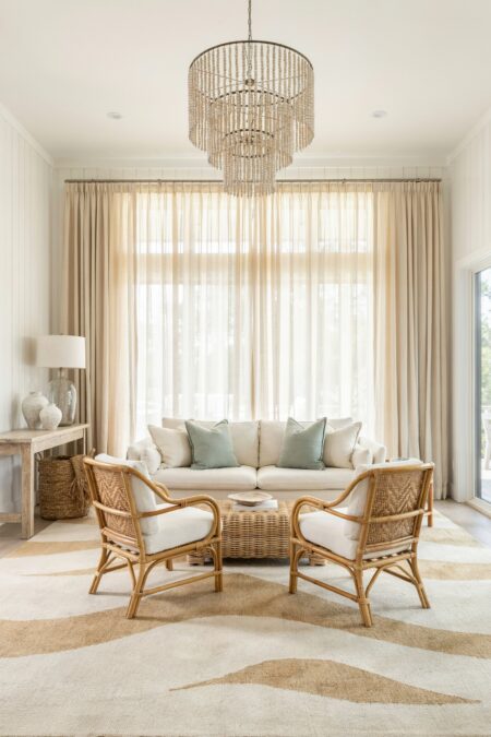 modern beach house living room with rattan armchairs, a wicker coffee table, a distressed console table, and sand tones in curtains and rug