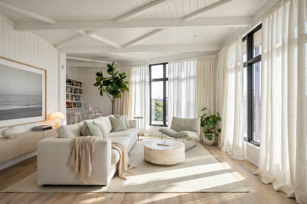 modern beach house living room with white shiplap walls, a cream sofa with pale light sage green pillows, a floating console, and sheer curtains